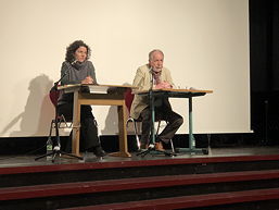 Das Foto zeigt Eike Besuden und die Schauspielerin Franziska Mencz an einem Tisch sitzend auf der Bühne der Aula des TGG.