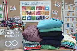 Das Foto zeigt die ersten Spenden von Second-Hand-Kleidung vor den Stellwänden im Foyer mit den Projektbeschreibungen.